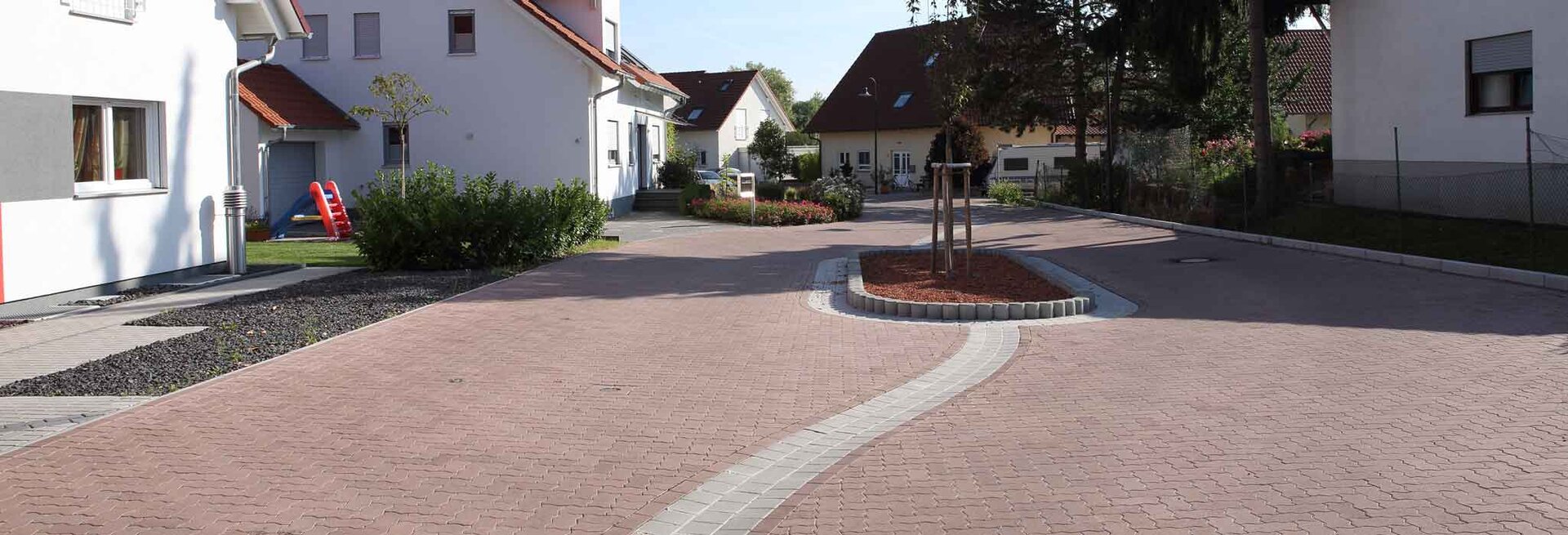 Wohngebiet mit Straße aus roten Pflastersteinen und Einfamilienhäusern im Hintergrund